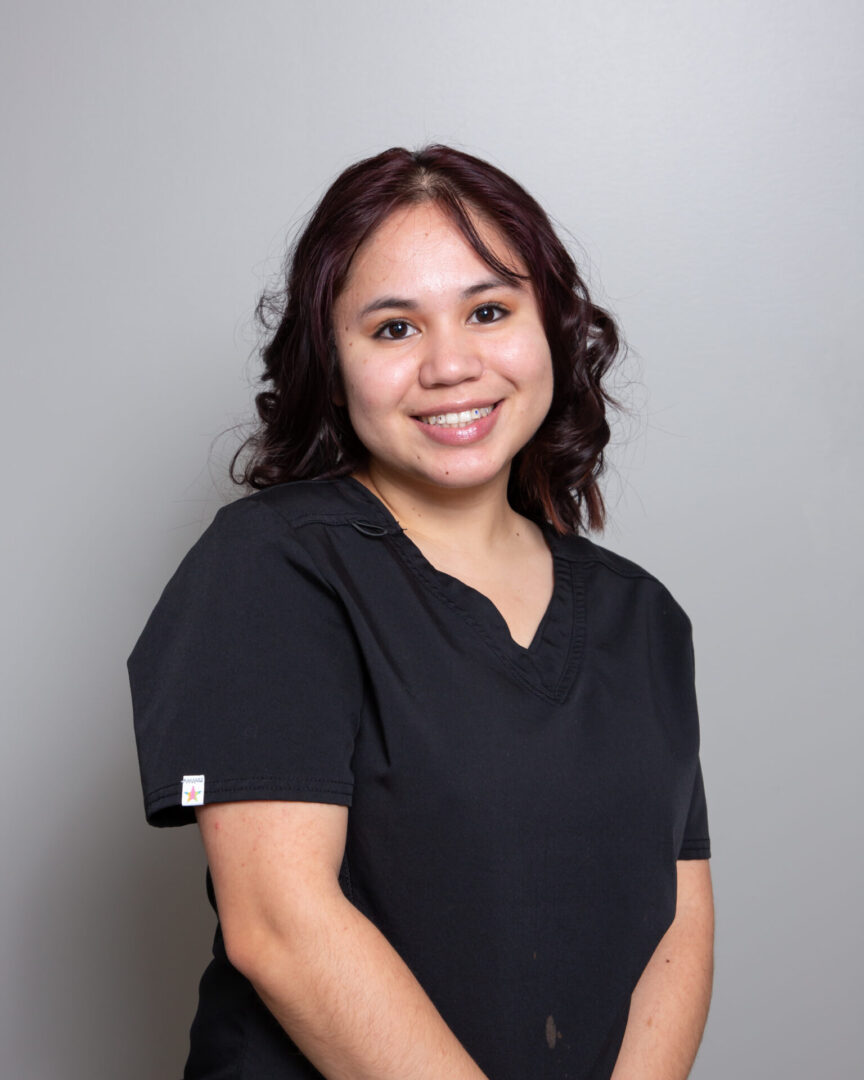 Smiling woman in scrub top, gray background.