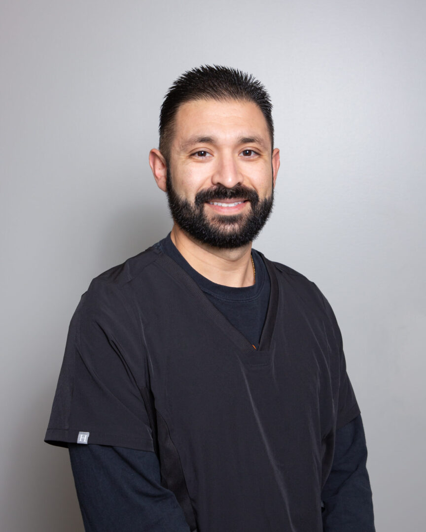 Smiling man in medical scrubs against gray background.