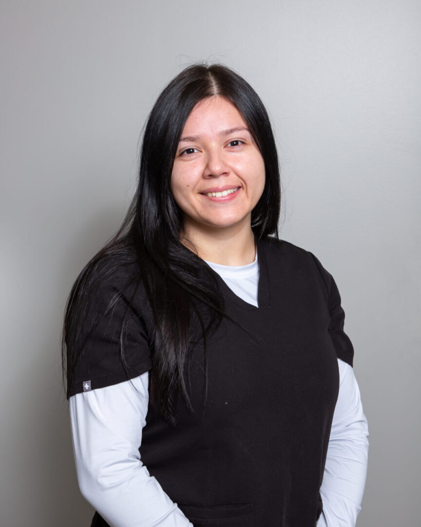 Smiling woman in medical attire, neutral background.